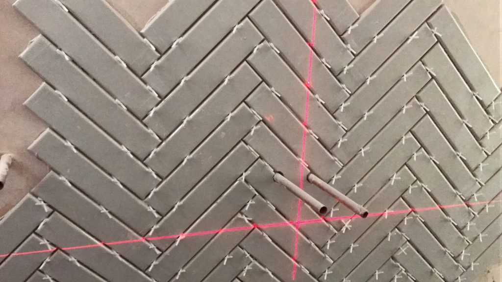 close-up herringbone ceramic bathroom wall tiling with spacers and pipe outlets Worcester
