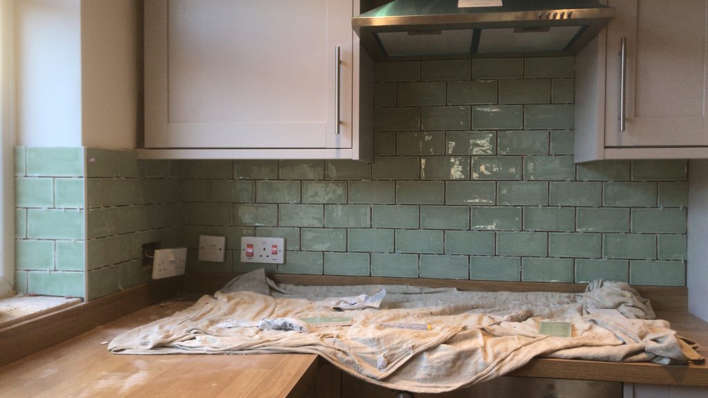 green porcelain kitchen tiles showing the cooker hob and splash with a dust sheet on the cooker for protection.