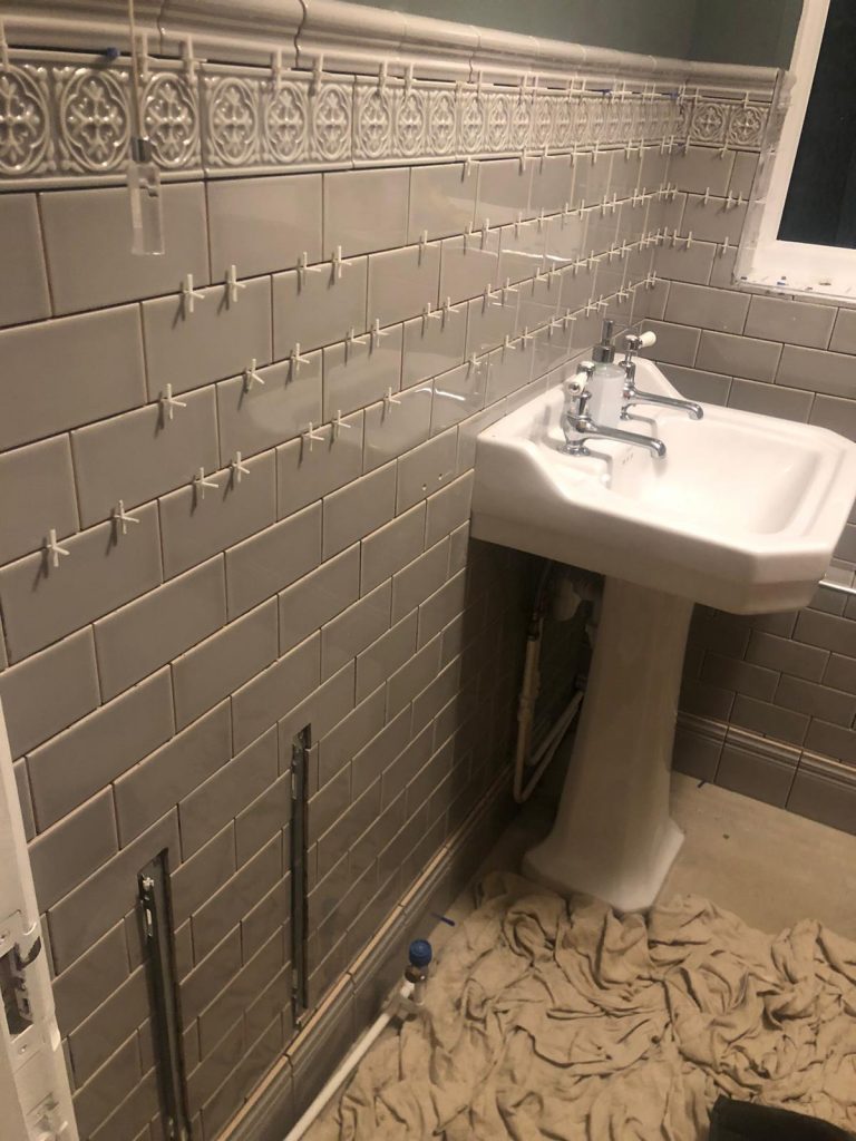 
Decorative porcelain wall tiles installation in a small bathroom showing spacers and protective dust sheets.
