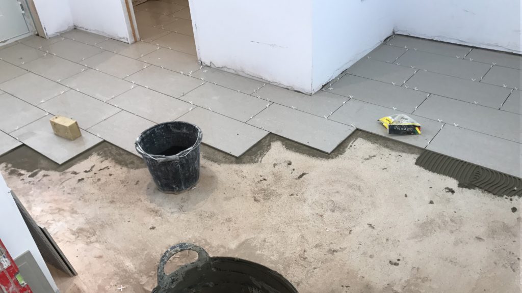 Partly installed kitchen floor tiles showing a bucket and sponge along with a bag of spacers