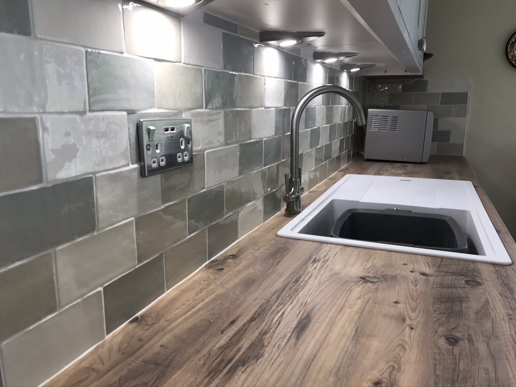 Decorative multi coloured wall tiles showing sink splash and long view image of worktops and tiled wall.