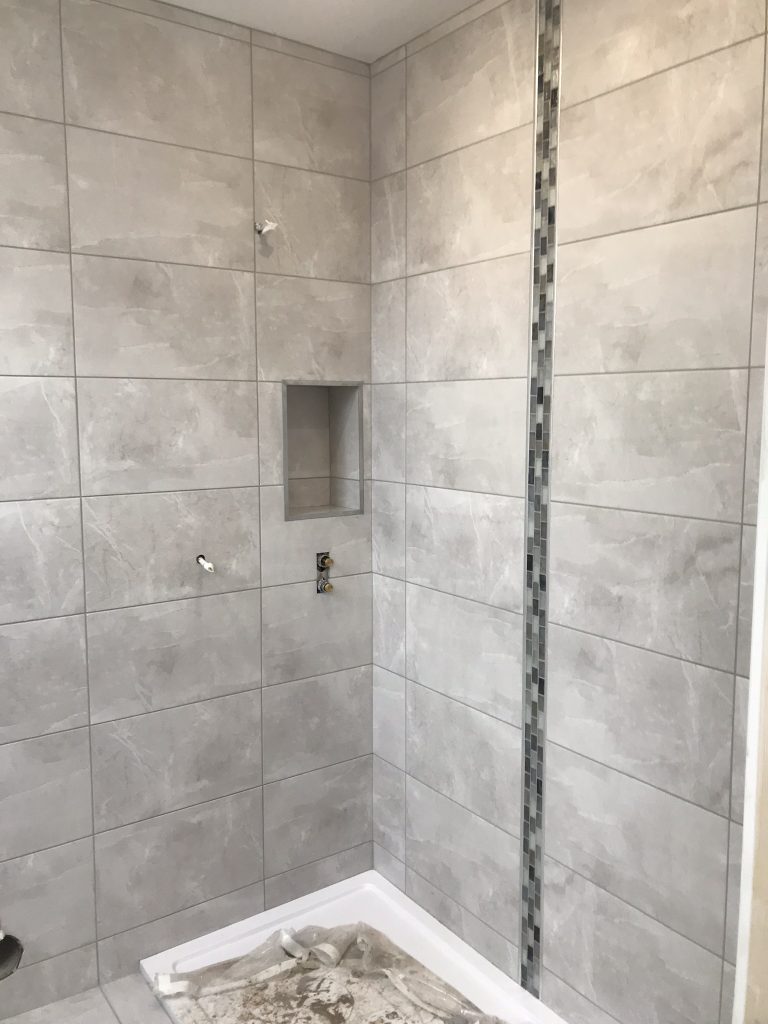 Grey stone look alike porcelain tiles with a mosaic feature column and a recess for shampoo bottles